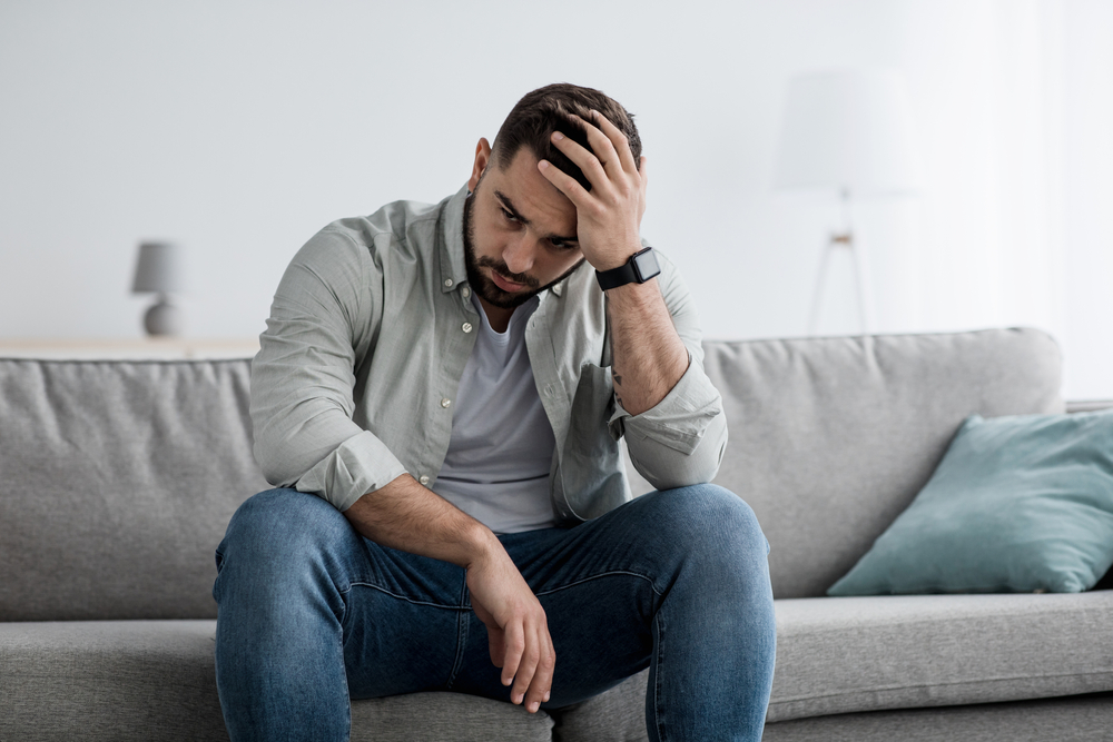 An upset man on a couch in an article on understanding a bulimia diagnosis on the Eating Disorder Recovery Specialists website.