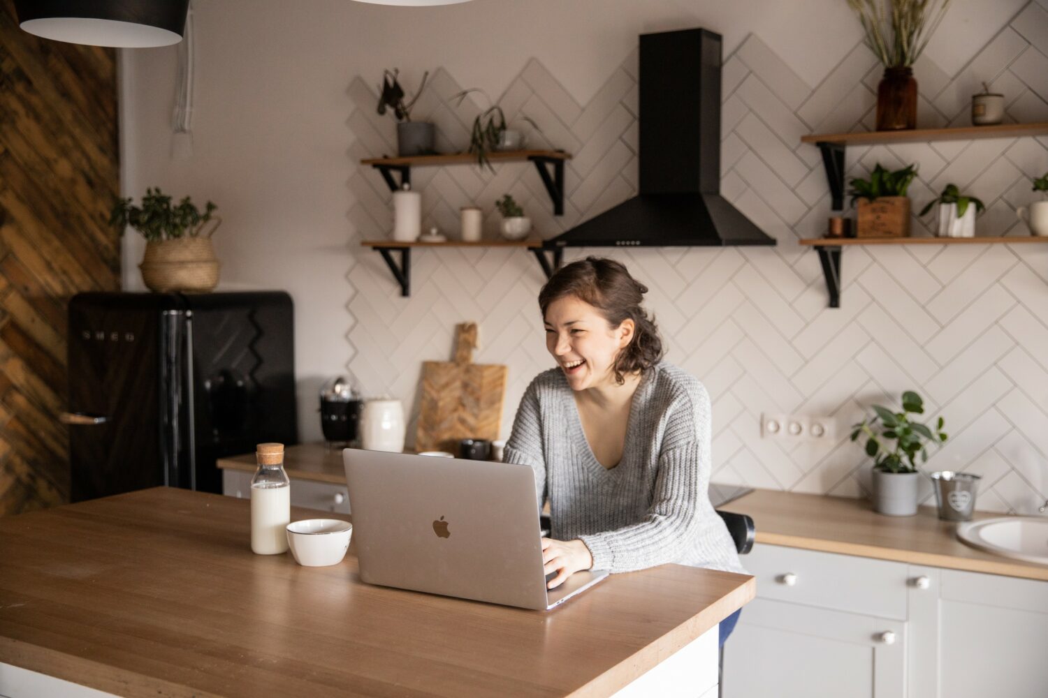 woman sitting at her kitchen table while laughing and on her laptop